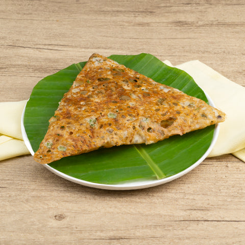 Triangular piece of Rava Dosa on a banana leaf and white plate, on a wooden surface.